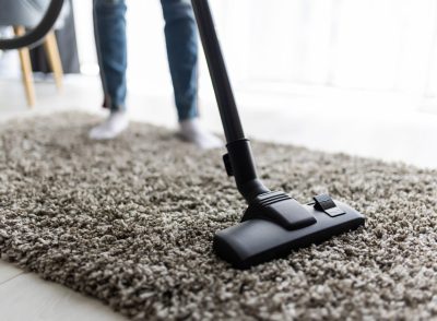 Close up of woman with legs vacuum cleaner cleaning carpet at home